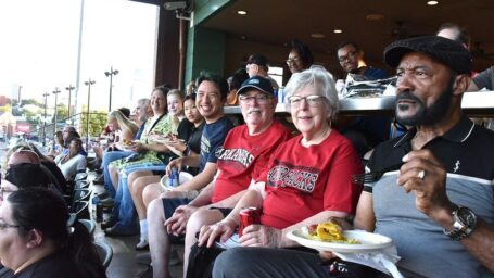 A group of people in stadium seats smiling at the camera.