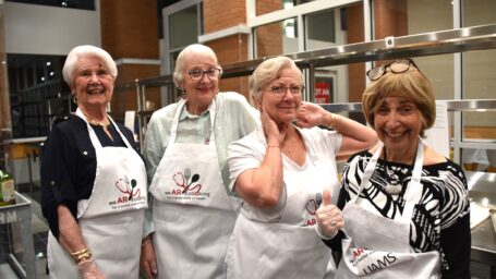 Four participants wearing UAMS-branded cooking aprons stand together in a kitchen setting, smiling and posing during the hands-on Culinary Medicine event.